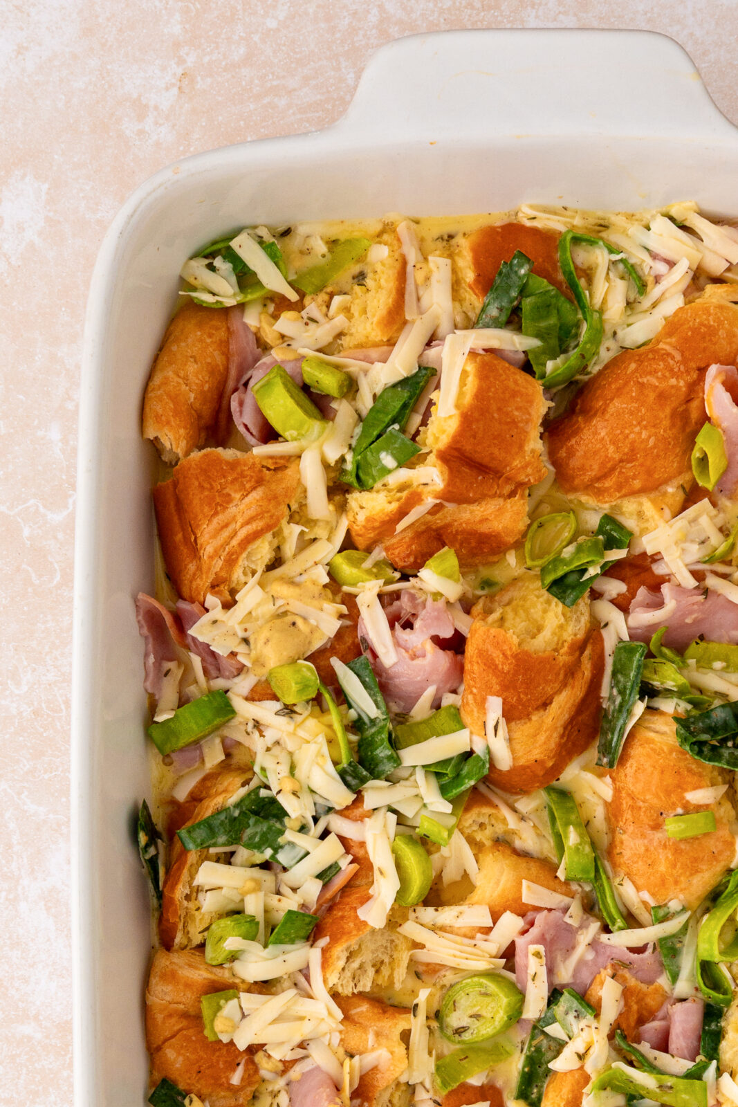 croissant pieces, ham, cheese and leeks in a baking dish
